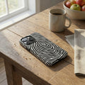 Phone case with black and white pattern on a wooden table with a mug and apples in the background