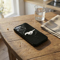 Black phone case with a logo on a wooden table next to a glass of water